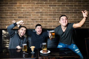 Young men drink beer, eat snaks and cheering for football. Winning emotions.