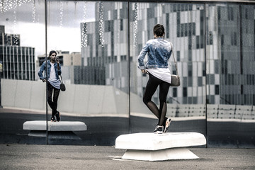 Portrait of young and stylish woman taking a selfie in front of the mirror wall in the park, Barcelona, Spain.