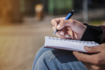 Man's hand writing on notebook, sketchbook outdoors