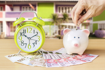 Piggy bank with money and alarm clock on wood table background ,hand add coin to piggy bank save...