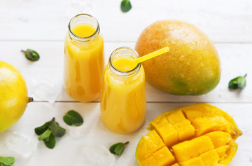 Fresh juice of a mango smoothies in a glass bottle and ripe mango fruit on a white wooden background.