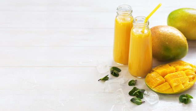 Fresh juice of a mango smoothies in a glass bottle and ripe mango fruit on a white wooden background.