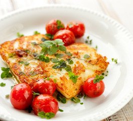 Grilled halloumi cheese with herbs and cherry tomatoes on a white plate