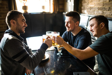 Meeting with the best friends. Three happy young men in casual wear talking and drinking beer while sitting in bar together