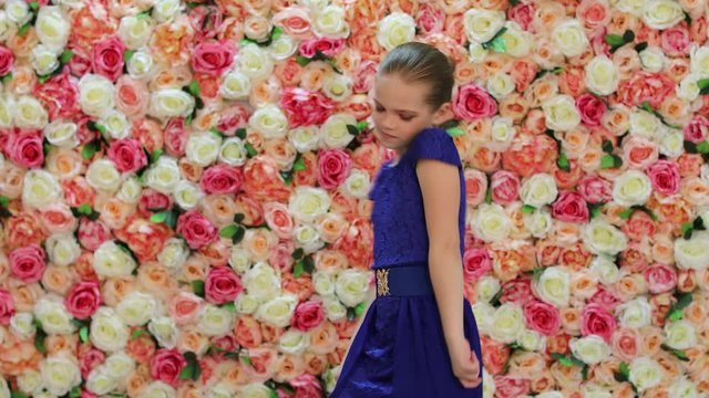 Dancer Girl. Beautiful little girl in a blue dress is dancing in the studio on a background of a floral wall