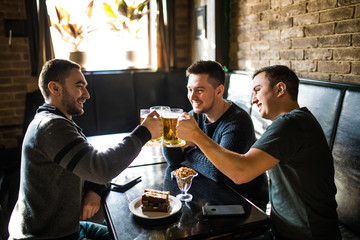 Meeting with the best friends. Three happy young men in casual wear talking and drinking beer while sitting in bar together