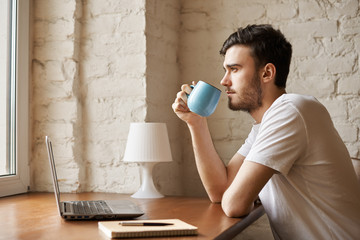 Cropped image of handsome copywriter with stylish beard holding cup with coffee in hand. Close up...