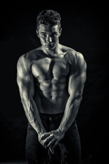 Fototapeta na wymiar Handsome young muscular man shirtless wearing jeans, isolated on black background in studio shot