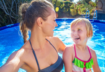 smiling healthy mother and child in swimming pool taking selfie