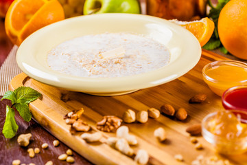Oatmeal porridge with nuts, jam and fruits on wooden board