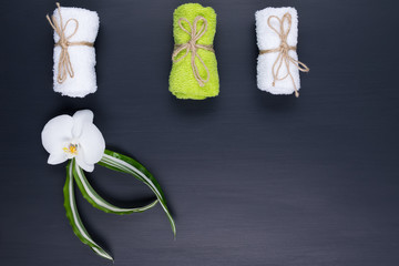 Three different towels are lying on a black background and a white orchid