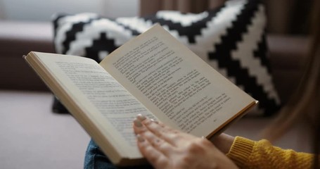 Close up woman hands reading interesting book while sitting on the couch at home. Close up back view. Close up book - Powered by Adobe