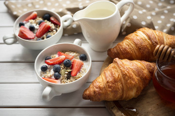 Cereals breakfast with seeds, oats,yogurt, milk, strawberry, blueberry,honey and fresh bakery on white wooden table.Breakfast table