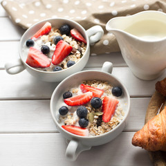 Two bowls with cereals breakfast with seeds, oats,yogurt,strawberry and blueberry on white wooden table.