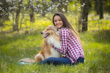 young beautiful woman with long hair sits on the lawn with collie dog. Outdoors in the park.