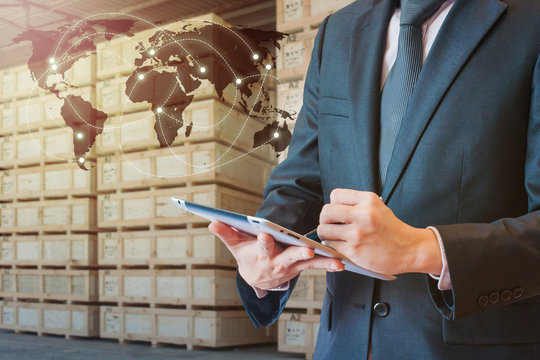Businessman touching tablet for analyze and checking stock at logistics port with blurred cargo warehouse transportation trading business concept, world map element of this image furnished by NASA
