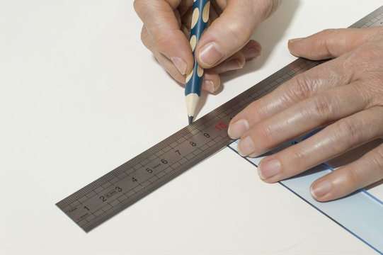 Una persona con el l&aacute;piz en la mano,utiliza una escuadra y una regla sobre un papel