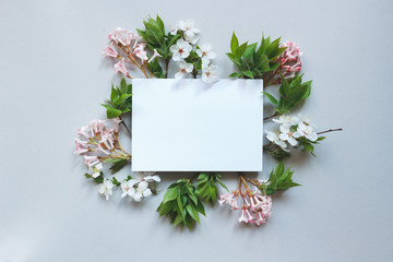 Spring background with paper sheet. Beautiful fresh flowers and leaves on gray background