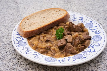 Roasted lamb livers with onion and wine sauce. Livers are chopped on the small pieces, roasted with black pepper, salt, wine and onion and served with slice of artisan bread on the old rustic plate. 