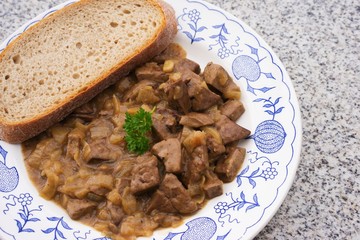 Roasted lamb livers with onion and wine sauce. Livers are chopped on the small pieces, roasted with black pepper, salt, wine and onion and served with slice of artisan bread on the old rustic plate. 