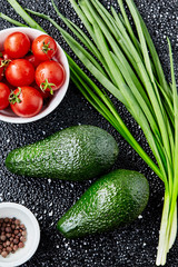 Fresh vegetables on a dark background- avocado, cherry tomatoes, cucumber, spring onions and spices.top view