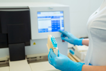 Hands of laboratory assistant loading sample tubes for coagulation test analysis and inputing data to coagulation machine