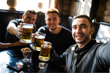 happy male friends drinking beer and taking selfie with smartphone at bar or pub