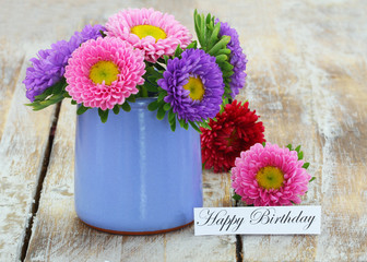 Happy Birthday card with colorful daisy flowers in blue pot on rustic wooden surface
