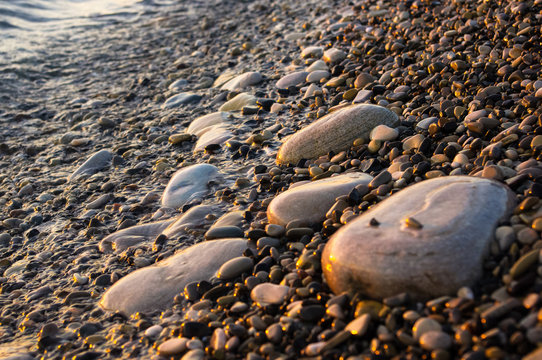 Fototapeta sea pebble beach with multicoloured stones, waves with foam