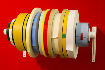 Variety double adhesive tape in; rolls of different types of tape with red background