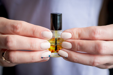 cuticle oil and manicure. Female hands with light shining manicure hold small bottle with oil