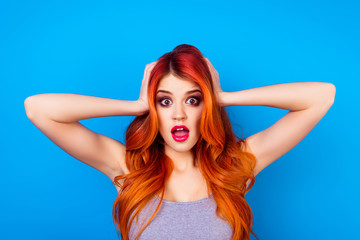 Obraz premium Close-up of attractive cute girl with long ginger ombre fair hair with shocked face touching head with hands while standing on blue background