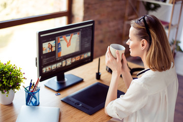 Female graphic designer sitting near screen and graphic tablet at the desktop in workstation and...