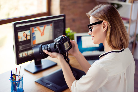 Side view  of female freelancer photographer cheking  photos on a digital camera while sitting at the table in workstation