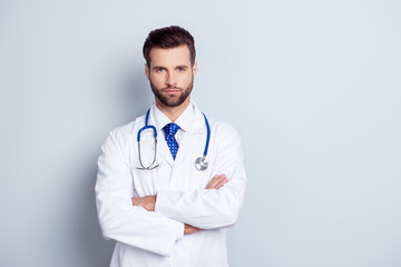Portrait of serious handsome male doctor with crossed hands on gray background
