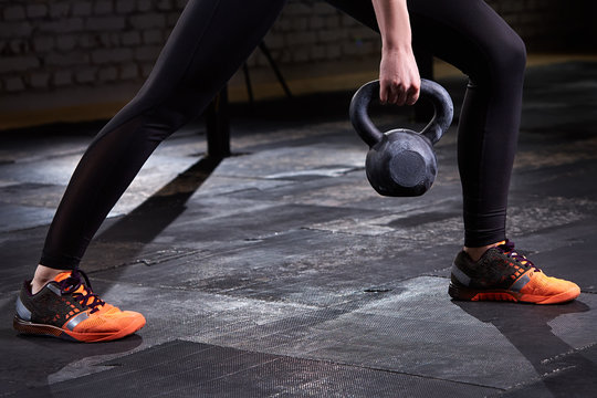 Closeup photo of young woman's legs in leggings and sneackers and kettlebell against dark background.
