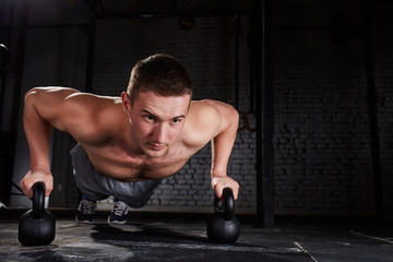 Sportsman doing push-ups exercise with kettlebell in a crossfit workout against brick wall