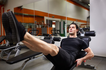 Fototapeta na wymiar Muscular man in the black sportwear doing push-ups with legs in a gym against mirror.