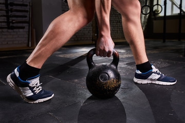 Obraz na płótnie Canvas Close-up photo of man's legs and arm while holding kettlebell on the gym floor against dark background.