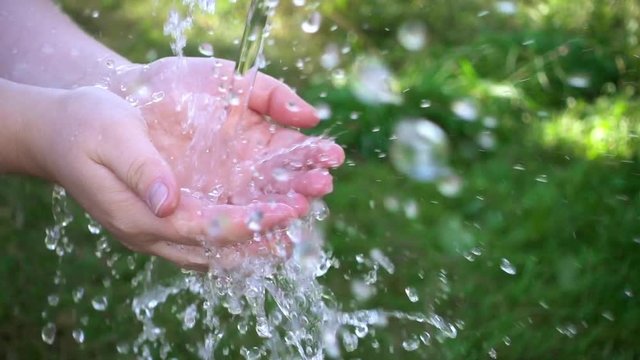 Water pouring in woman's hands. Green grass nature background, environment issues. Slow motion