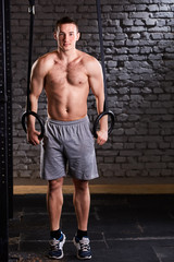 Sportsman doing pull ups with gymnastic rings for strength and crossfit exercise against brick wall.