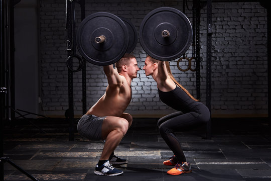 Crossfit lifting bar by woman and man in group workout against brick wall.