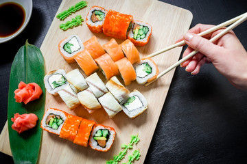 Set of sushi rolls, sauce, wasabi and hand with chopsticks on dark background. Top view. Flat lay. Japanese food
