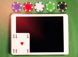 Top view, white tablet, various colors poker chips and aces on screen