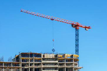 Construction site. Construction cranes and high-rise building under construction against blue sky.