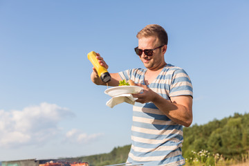 Junger Mann auf einem Picknick gibt Senf zu seinem Grill-Teller