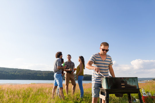 Gruppe von jungen M&auml;nnern und Frauen beim Grillen am See im Sommer