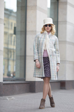 A beautiful stylish blond woman in a coat and hat and sunglasses on a city street.