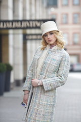 Beautiful stylish blond woman in coat and hat on city street.