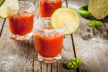 Mexican traditional alcohol drink. Sangrita, with tequila, tomato juice, hot spices, chili and lime.Analogous bloody mary. On rustic wooden table, copy space